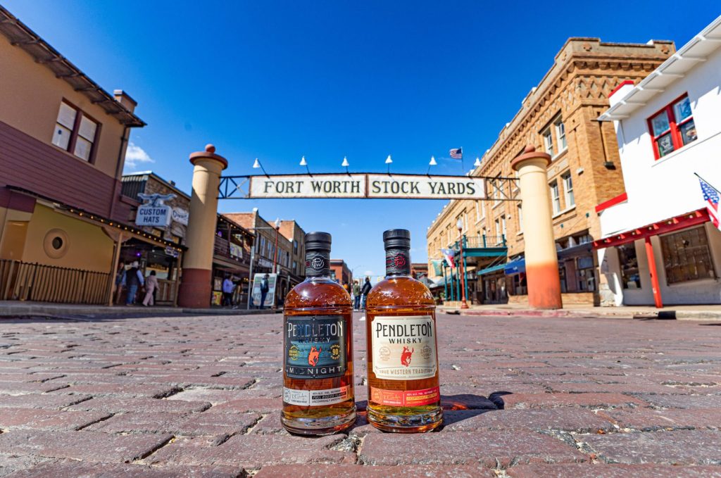 Pendleton Whisky Midnight and Pendleton Whisky bottles on the brick street beneath the Fort Worth Stock Yards sign