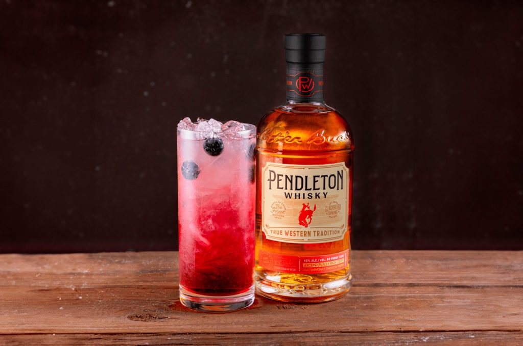 Stars and Stripes Lemonade cocktail with blueberries beside a bottle of Pendleton Whisky